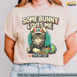 May include: Beige t-shirt with a grumpy cat wearing bunny ears and the text "SOME BUNNY LOVES ME". An open Easter egg with colourful candies is next to the cat. The text "IT'S MY CAT" is below the image.