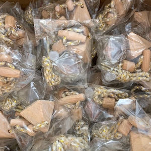 May include: A close-up of a pile of small, wooden, triangular-shaped ornaments with gold and white string attached. The ornaments are packaged in clear plastic bags.