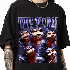 May include: Black t-shirt featuring a graphic of several whimsical worm-like creatures with red scarves and blue fur. The text "THE WORM" is displayed above the creatures in a blue, stylized font.