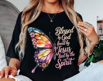 May include: Black t-shirt featuring a colorful butterfly design with orange, pink, yellow, and blue hues. The text "Blessed by God loved by Jesus leed by the Spirit" is written in a script font.