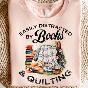 May include: A pink t-shirt with the text "Easily Distracted by Books & Quilting" in black. The design features a stack of books, a quilt, and a basket of flowers.