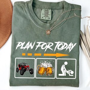 May include: Green t-shirt with the text "Plan for Today" in white. The shirt has three white boxes with illustrations of an off-road vehicle, two beer mugs, and a person in a suggestive pose.