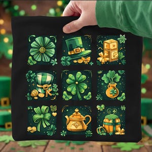 Puede incluir: Bolso tote negro con una cuadrícula de ilustraciones temáticas del Día de San Patricio. Los diseños incluyen un lazo verde, un sombrero de duende, un trébol de cuatro hojas y una tetera. Las ilustraciones son en tonos verdes y dorados.