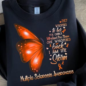 May include: Black sweatshirt with an orange butterfly and the text "They whispered to her you cannot withstand the storm she whispered back I am the storm" with an orange ribbon. The text "Multiple Sclerosis Awareness" is at the bottom of the sweatshirt.