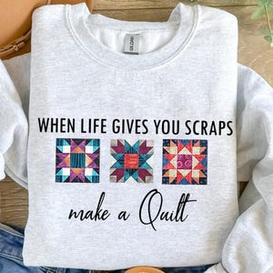 May include: A gray sweatshirt with the text "When life gives you scraps make a quilt" and three colorful patchwork quilt squares.