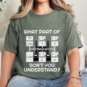 May include: A green t-shirt with a white graphic of a semi-truck transmission gear shift pattern. The text "WHAT PART OF" and "DON'T YOU UNDERSTAND?" is printed on the shirt.
