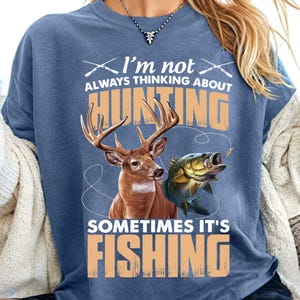 Peut inclure: Un t-shirt bleu avec un motif blanc qui dit "Je ne pense pas toujours à la chasse, parfois c'est la pêche". Le motif représente également un cerf et un poisson.