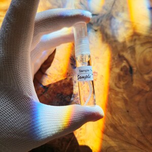 May include: A clear glass bottle with a white label that says "Sample To Sample" is held in a white gloved hand. The bottle is filled with a clear liquid.