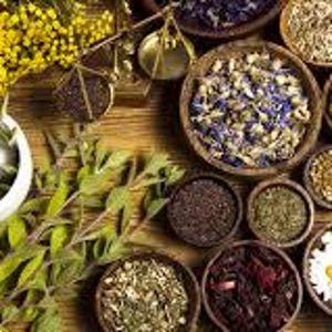 May include: A collection of dried herbs and flowers in small bowls, arranged on a wooden surface. The herbs and flowers are a variety of colors, including green, brown, yellow, and purple. There is also a white mortar and pestle in the image.