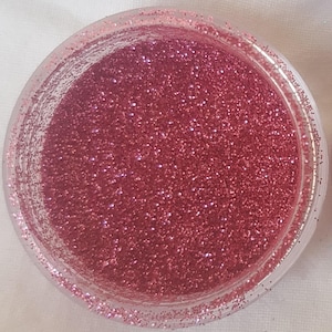 May include: A close-up view of a small jar filled with fine pink glitter.