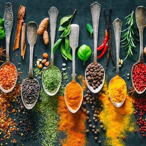 May include: A collection of various spices and herbs in silver spoons on a dark background. The spices include cloves, mustard seeds, paprika, black peppercorns, green peppercorns, turmeric, cumin, rosemary, and cardamom.
