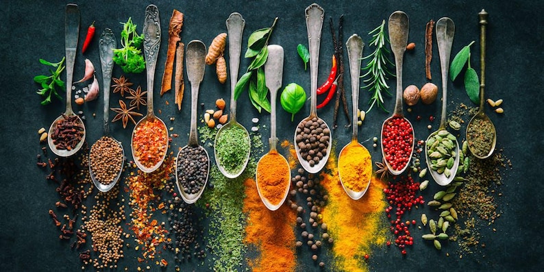 May include: A collection of various spices and herbs in silver spoons on a dark background. The spices include cloves, mustard seeds, paprika, black peppercorns, green peppercorns, turmeric, cumin, rosemary, and cardamom.