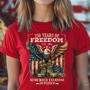 May include: Red t-shirt with a patriotic design. The graphic features an eagle with American flag wings, combat boots, and the text "250 YEARS OF FREEDOM 1776-2026" and "REMEMBER EVERYONE DEPLOYED".