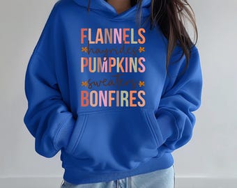 May include: A vibrant blue hoodie with a front pocket and a hood with drawstrings. The front displays the words "FLANNELS, HAYRIDES, PUMPKINS, SWEATERS, BONFIRES" in a colourful, autumn-themed font, with small floral accents. A casual, seasonal garment.