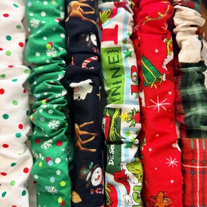 Peut inclure: Plusieurs chouchous en tissu avec des motifs de Noël. Les motifs comprennent des pois, des flocons de neige, des rennes, des bonhommes de neige, des personnages du Dr. Seuss et du tartan. Les chouchous sont rouges, verts, blancs et noirs.
