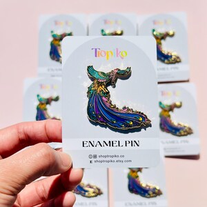Puede incluir: Un pin de esmalte colorido con un p&aacute;jaro estilizado con una cola larga y fluida. El pin est&aacute; en una tarjeta blanca con el texto "Tropiko Enamel Pin" y la direcci&oacute;n del sitio web "shoptropiko.co".