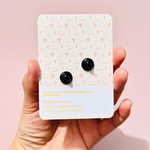 May include: A white card with a repeating pattern of pink and orange sun and wave designs. The card has instructions on how to use a magnetic pin converter: "REMOVE pin backs, SLIDE the magnetic locks, STICK to magnetic surface".