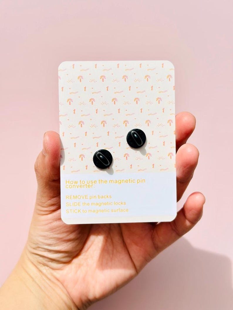 May include: A white card with a repeating pattern of pink and orange sun and wave designs. The card has instructions on how to use a magnetic pin converter: "REMOVE pin backs, SLIDE the magnetic locks, STICK to magnetic surface".