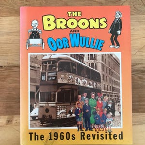 Pode incluir: Uma capa de livro com fundo laranja que apresenta uma ilustração de desenho animado de um grupo de pessoas em pé na frente de um ônibus de dois andares. O título do livro é "The Broons and Oor Wullie: The 1960s Revisited".