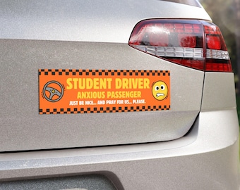 May include: Orange rectangular bumper sticker with the text "STUDENT DRIVER ANXIOUS PASSENGER JUST BE NICE... AND PRAY FOR US... PLEASE." Features a steering wheel icon and a worried face emoji. The sticker is on the back of a silver car.