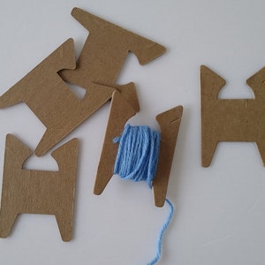May include: Four cardboard yarn holders with a blue ball of yarn on one of the holders. The yarn holders are shaped like a capital H.