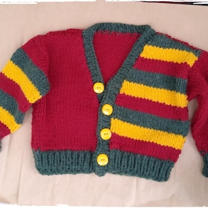 May include: A handmade, knitted cardigan in a vibrant color scheme. The body is a deep red, with sleeves featuring alternating stripes of yellow and teal. The cardigan has a teal collar, cuffs, and hem, and is fastened with yellow buttons. A cozy, colorful garment.