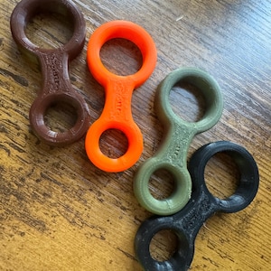 May include: Four different colored plastic rings, each with two loops. The rings are brown, orange, green, and black.
