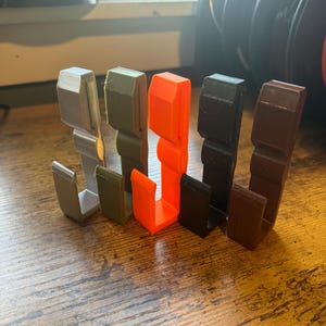 May include: Five different colored plastic hooks, arranged in a row from left to right: silver, green, orange, black, and brown.