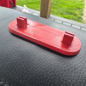 Könnte beinhalten: Ein rotes 3D-gedrucktes Objekt mit zwei erhöhten Abschnitten an beiden Enden. Das Objekt liegt auf einer schwarzen Oberfläche.