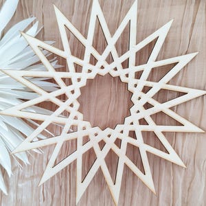 Può includere: Una grande stella a 12 punte in legno con un design geometrico. La stella è di colore marrone chiaro e ha una finitura in legno naturale.