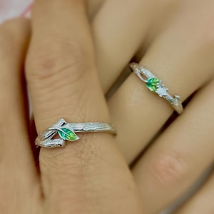 Könnte beinhalten: Zwei silberne Ringe mit einem Zweigdesign und grünen Emailleblättern. Ein Ring hat einen kleinen klaren Stein.