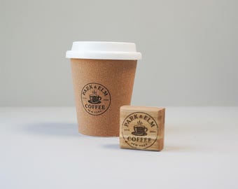 May include: A cork-covered to-go coffee cup with a white lid and a black logo that says "Park & Elm Coffee Est. 2019 New York" with a stylized image of a coffee cup. A small wooden block with the same logo is next to the cup.