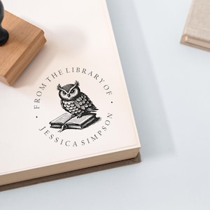 May include: A round, white, self-inking stamp with a black and white illustration of an owl perched on a book. The text around the owl reads "From the Library of Jessica Simpson."