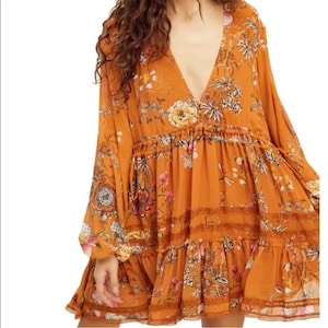 May include: An orange-colored dress with a deep V-neck and long sleeves. The dress features a floral pattern in shades of pink, yellow, and white. The dress has a tiered skirt and lace detailing.