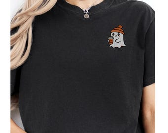 May include: Black t-shirt featuring a cute cartoon ghost wearing a brown beanie and holding a coffee cup. The ghost has a smiling face. The t-shirt is a dark charcoal color and has a crew neck.