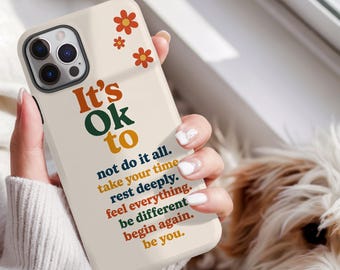 May include: A cream-colored smartphone case featuring orange flower icons and the text: It's Ok to not do it all. take your time rest deeply. feel everything. be different begin again. be you. The case has a cutout for a triple-lens camera system.