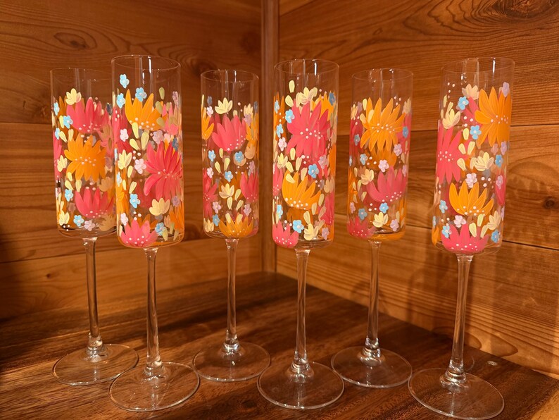 Pu&ograve; includere: Un set di sei fl&ucirc;te da champagne in vetro trasparente con un motivo floreale dipinto a mano in tonalit&agrave; vivaci di arancione, rosa, giallo e azzurro. Ogni bicchiere alto e sottile presenta uno stelo lungo e una base circolare con decori.