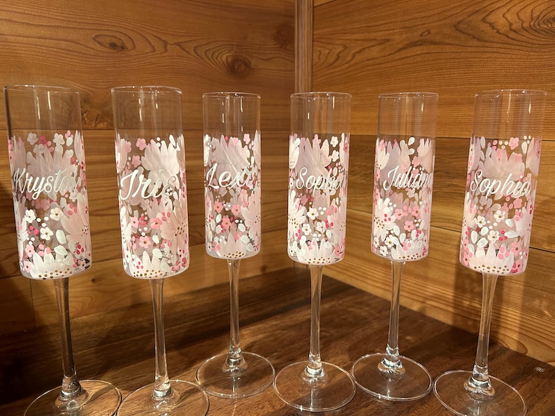 Pu&ograve; includere: Sei fl&ucirc;te da champagne in vetro trasparente con un motivo floreale dipinto a mano nei toni del rosa, bianco e rosso chiaro. Ogni fl&ucirc;te &egrave; personalizzato con un nome in corsivo bianco: Krystal, Iris, Lexi, Sophia, Juliana e Sophia.