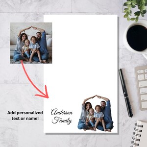 May include: A white notepad with a family photo and the text "Anderson Family" in elegant script. The image shows a family of four with their arms forming a roof shape. The notepad is on a marble surface.