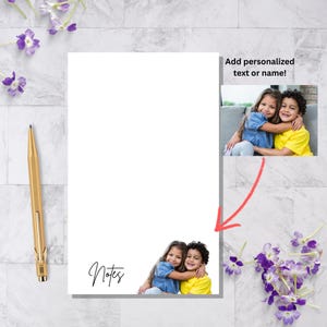 May include: White notepad with the word "Notes" in script. The notepad has a photo of two children hugging. The image also includes a gold pen and purple flowers. Text on the notepad says "Add personalized text or name!"