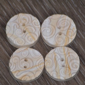 Puede incluir: Cuatro botones blancos con un patrón de espiral. Los botones tienen dos agujeros cada uno.