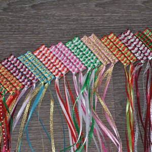Puede incluir: Un conjunto de 12 marcapáginas de cinta tejida de colores vivos con cintas largas y colgantes en varios colores, incluidos rojo, verde, blanco, dorado y azul.