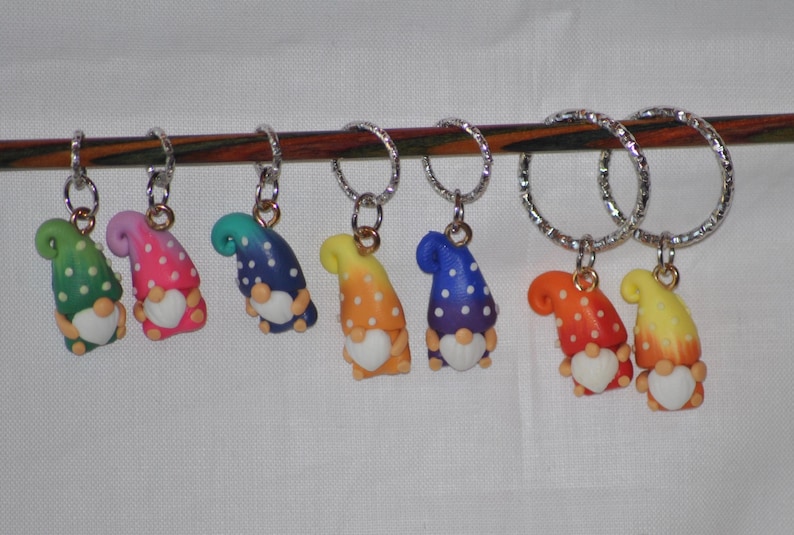 Puede incluir: Conjunto de ocho marcadores de punto de gnomo coloridos con lunares blancos y un coraz&oacute;n blanco. Los gnomos est&aacute;n unidos a anillos plateados.