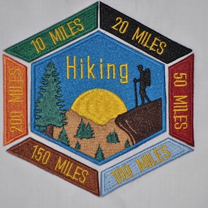Puede incluir: Un parche hexagonal con un centro azul que presenta una silueta de excursionista, un sol y árboles. El parche tiene seis secciones naranja, roja, verde, negra y azul con el texto "Hiking" y incrementos de millaje: 10 millas, 20 millas, 50 millas, 100 millas, 150 millas y 200 millas.