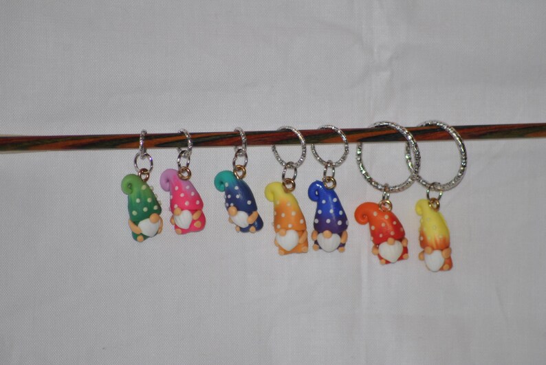 Puede incluir: Siete marcadores de punto de gnomo coloridos con lunares blancos y un coraz&oacute;n blanco en cada gnomo. Los marcadores de punto de gnomo est&aacute;n colgados en una varilla de madera.