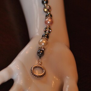 May include: A delicate bracelet with a silver ring charm, featuring alternating white pearls, pink beads, and dark gray beads.