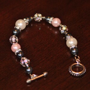 May include: A bracelet with white and pink pearls, black beads, and silver accents. The bracelet has a toggle clasp.
