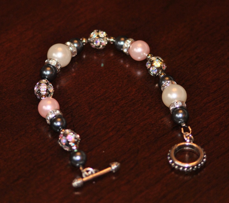 May include: A bracelet with white and pink pearls, black beads, and silver accents. The bracelet has a toggle clasp.