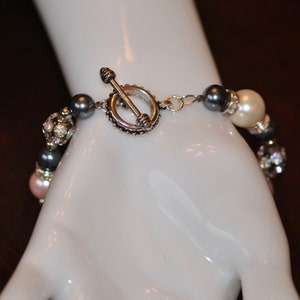 May include: A multi-strand bracelet with gray, white, and pink beads, and a silver toggle clasp.