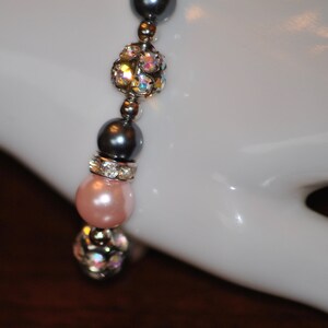 May include: A bracelet with pink, gray, and clear beads. The beads are interspersed with silver spacers. The bracelet is on a white mannequin hand.